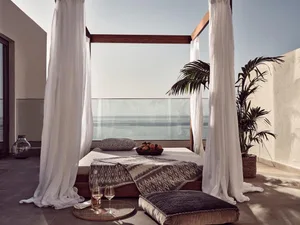 A modern bedroom featuring a bed with a canopy, white curtains, and a view of the ocean.