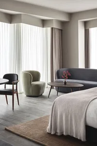 A modern bedroom featuring a cozy bed with textured fabrics, a grey sofa, and a round wooden table with a vase of flowers.