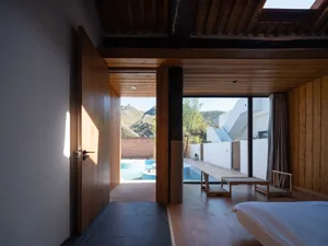 Spacious bedroom with modern design featuring wooden furniture and a view of a pool and mountains.