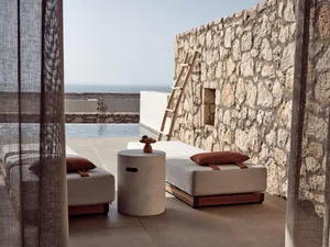Modern outdoor lounge furniture including plush seating, stone wall, and sea view.