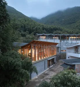 A modern house featuring glass and concrete textures surrounded by lush greenery, with a wave-shaped roof and open-air design