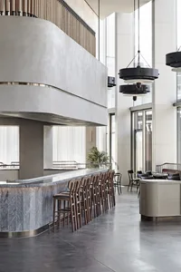 A modern industrial restaurant bar with concrete and marble surfaces, featuring wooden chairs and black pendant lights.
