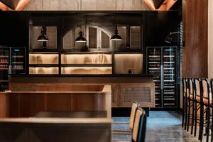 A modern industrial restaurant bar with wooden furniture, glass shelves, and hanging lights.