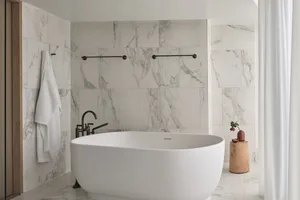 A modern minimalist bathroom with a freestanding bathtub, black faucet, and marble tiles.