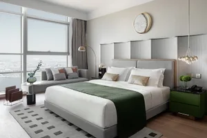 A modern minimalist bedroom with a gray bed, white linens, and a green throw blanket.