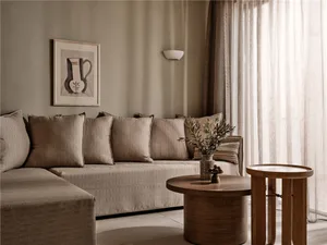 A modern minimalist living room featuring a corner sofa adorned with fabric cushions, a wooden side table with a green plant,
