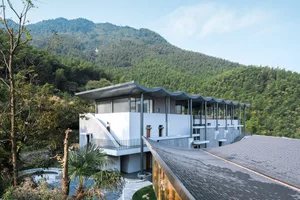 A modern residential building with concrete, glass, and wood exterior materials, surrounded by nature.