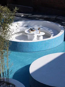 A circular poolside seating area with white and blue ceramic tiles, featuring tables and decorative elements.
