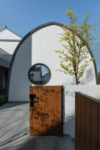 A wooden door with a keyhole and a small round window set in a white wall, with a tree nearby.