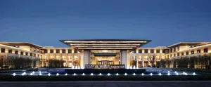 A modern hotel entrance with illuminated lighting, glass facade, and concrete pillars.