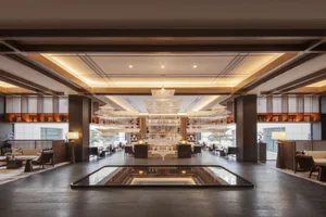 A modern hotel lobby with marble flooring, wooden beams, and a central water feature.
