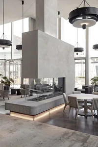A modern lobby featuring a concrete and glass fireplace, round dining tables, and chairs.