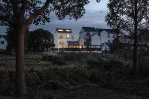 A modern residential building with white rendered stone exterior at dusk with lights on.