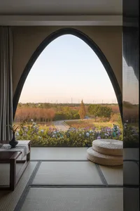 A living room interior framed by an arched window overlooking a serene outdoor landscape with wooden cushions on the floor, g