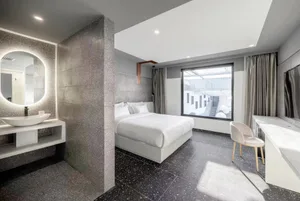 Modern, minimalist hotel room featuring glass walls, concrete flooring, and white textiles.