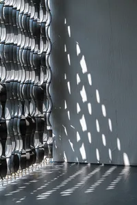 A minimalist interior design featuring metallic elements casting patterned shadows on the wall and floor.
