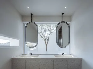 Modern bathroom with concrete countertops and two oval mirrors above a double sink.