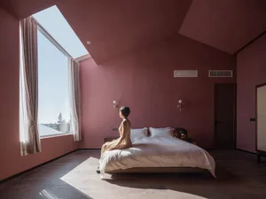 A modern bedroom with a wooden plank floor, a large bed with white linens, and a skylight in the ceiling.