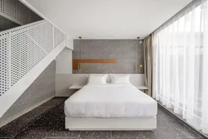 Modern bedroom with white bed, minimalist design, and textured grey wall behind the headboard.