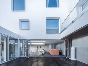 Modern living room with concrete walls, large floor-to-ceiling windows, and minimalist furniture.