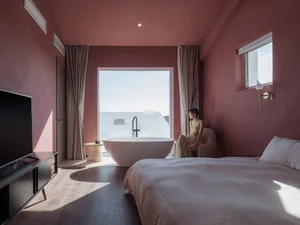 A modern bedroom with a marble freestanding bathtub, large window, and minimalist decor