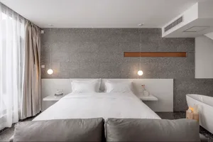 A modern minimalist bedroom featuring a grey concrete wall with floating nightstands and a white bed.