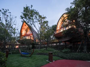 A modern residential wooden cabin with warm indoor lighting surrounded by trees.