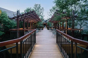 A modern outdoor restaurant with wooden pergolas and seating areas surrounded by greenery.