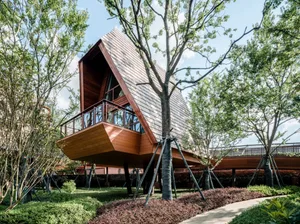 A modern residential treehouse with wooden exterior and a balcony surrounded by greenery.