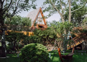 A modern wooden treehouse with a triangular roof and a hammock in a lush garden.