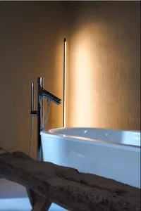 A simplistic bathroom featuring a sleek ceramic bathtub and a modern, minimalist sink faucet in a well-lit room.