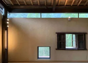 View of a room with an industrial design featuring concrete walls, wooden beams, and a window overlooking greenery.