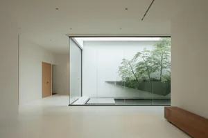 A minimalist interior space featuring large glass walls looking out onto a green courtyard.