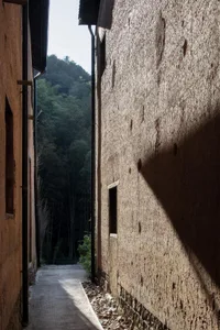 一條狹窄的老舊混凝土步道，兩側為石牆，陽光在牆面上投射出陰影。