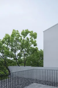 Modern, minimalist exterior with concrete walls and black railings, surrounded by greenery.