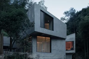 Modern concrete residential interior with large windows and warm lighting.