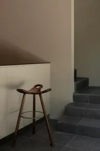 A minimalist hallway with a wooden stool near a staircase, featuring a plain color palette and simple design.