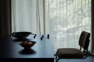 A photograph of a modern interior design featuring a window with a view of a serene landscape, a table with a bowl of fruit a