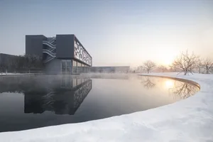 現代建築物被雪覆蓋，周遭景觀倒映在平靜的水面上