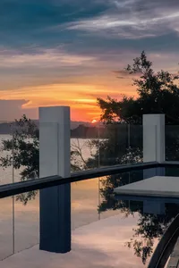 A stunning sunset reflection captured through a glass pool fence, showcasing serene water and scenic landscape.