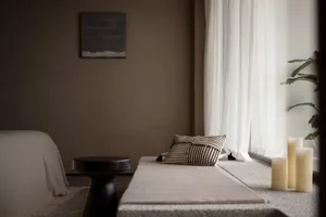 A minimalist bedroom featuring textured textiles on a window seat and a black stool.