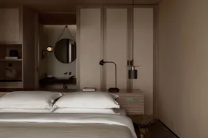 Modern minimalist bedroom with white bedding, wooden furniture, and a round mirror.