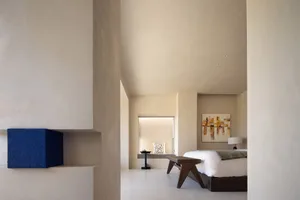 Modern bedroom with minimalist design, featuring a concrete wall, wooden furniture, and a high ceiling.