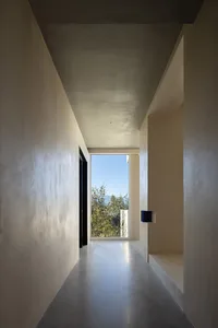 A minimalist hallway with concrete walls and a view of the outdoors through a large window.