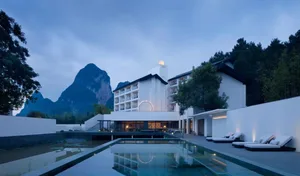 A minimalist hotel with white stone exteriors and black chevron patterns, featuring a water reflection pool.