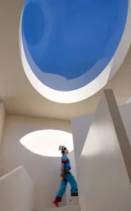 A modern architectural space with a concrete floor and walls, featuring a large circular opening in the ceiling.