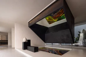 A modern interior featuring a black metal structure with a colorful abstract painting on the ceiling, set on a black tile pav
