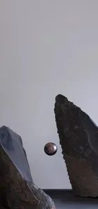 A metallic ball floating between two irregular rock formations against a plain white background.