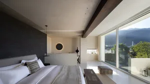 Modern minimalist bedroom featuring concrete flooring, white bedding, and a large window overlooking a scenic landscape.
