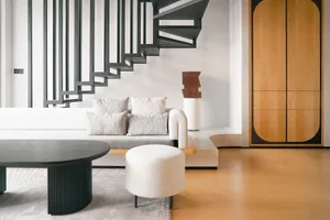 A modern minimalist living room featuring a concrete and metal staircase, a white and gray sofa, and a wooden cabinet.